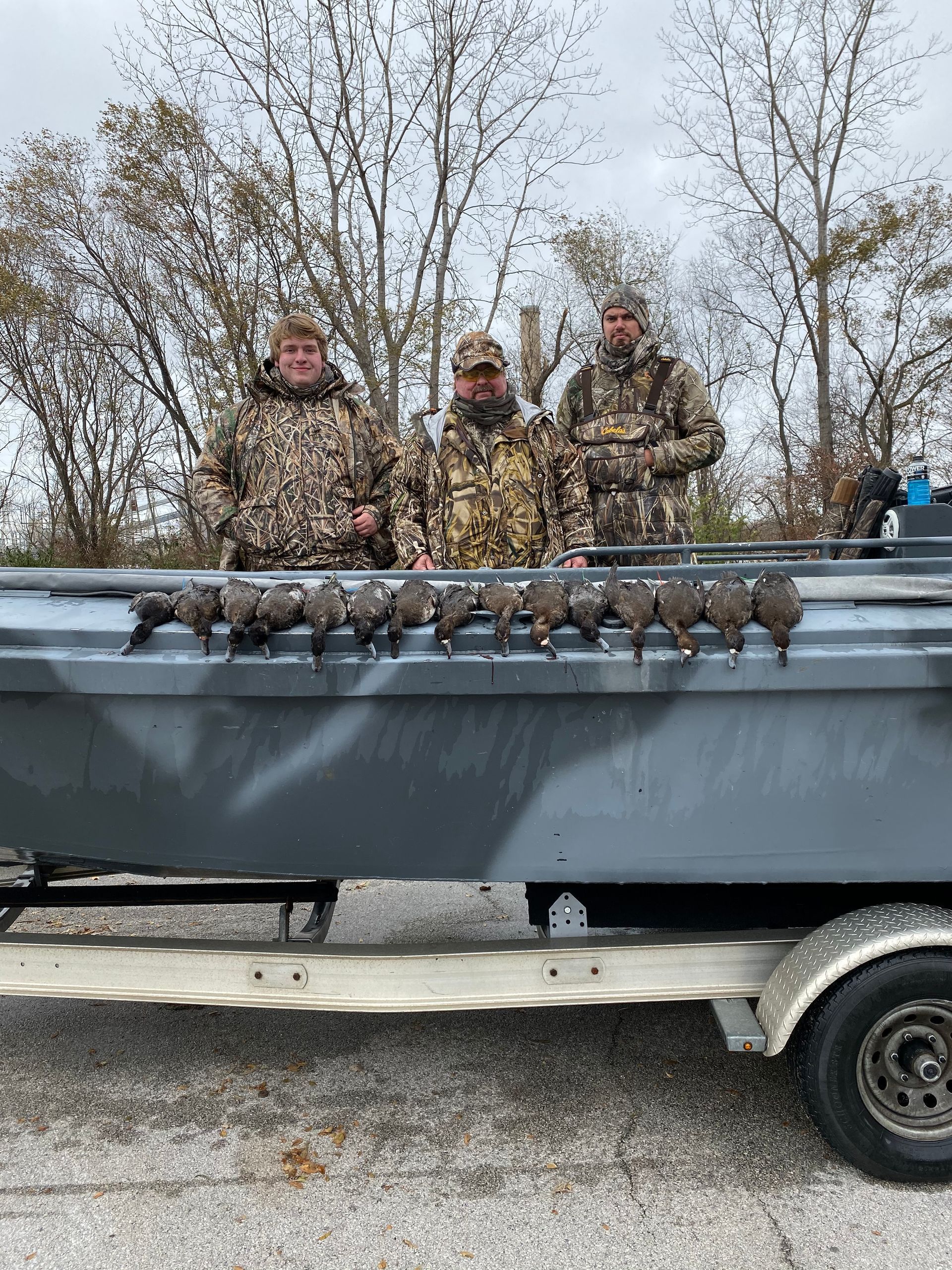 Three men are standing in the back of a boat filled with ducks.