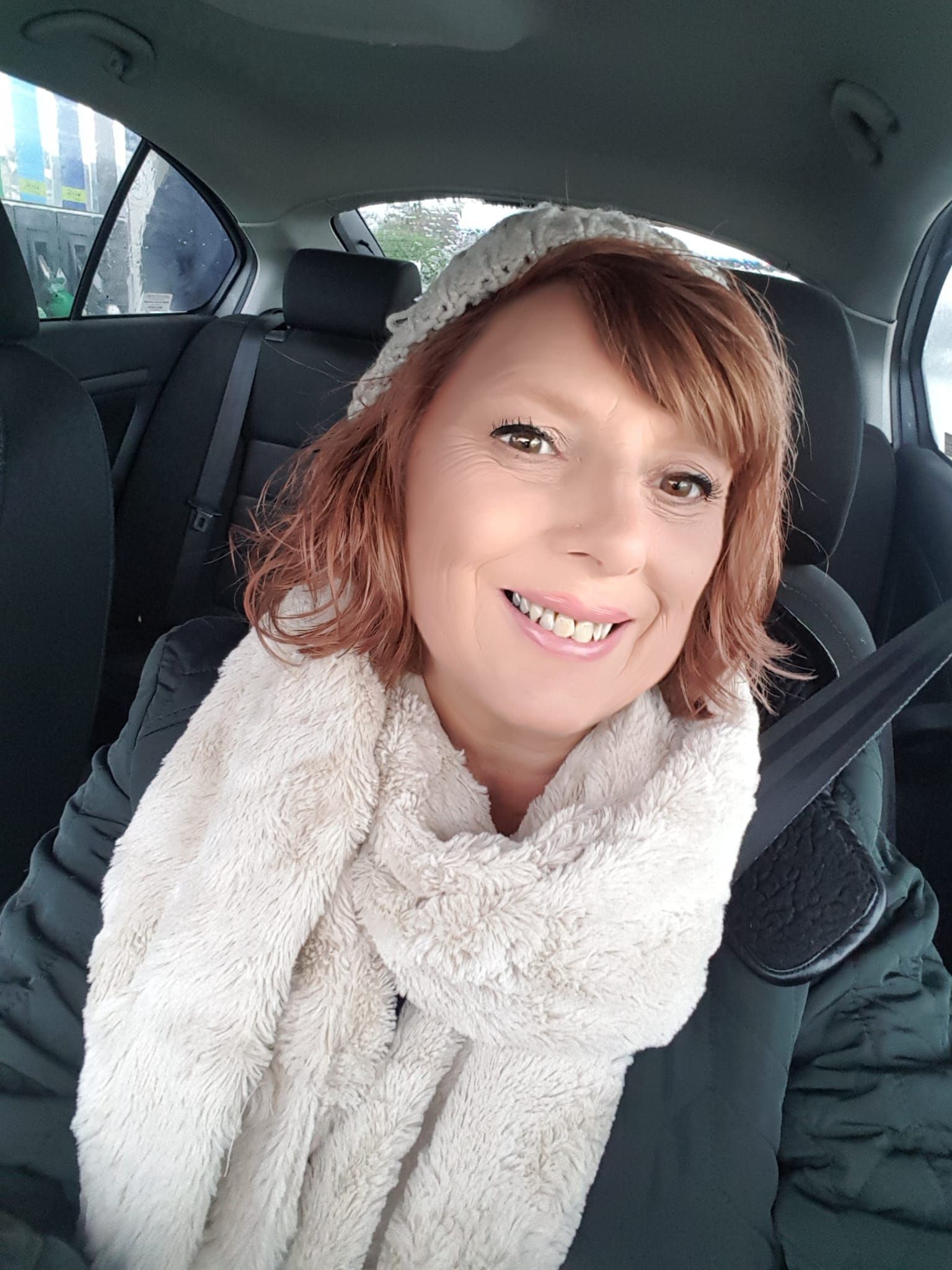A woman is sitting in the back seat of a car wearing a scarf and a hat.