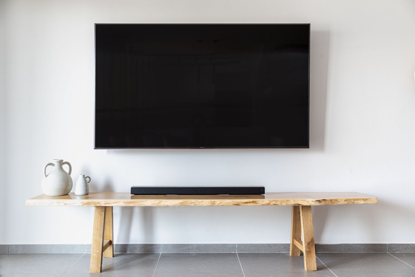 A flat screen tv is mounted to the wall above a wooden bench.