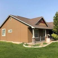 A brown house with a porch and a large lawn in front of it.