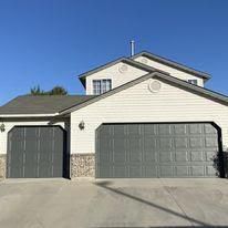 A white house with two garage doors and a blue sky in the background.