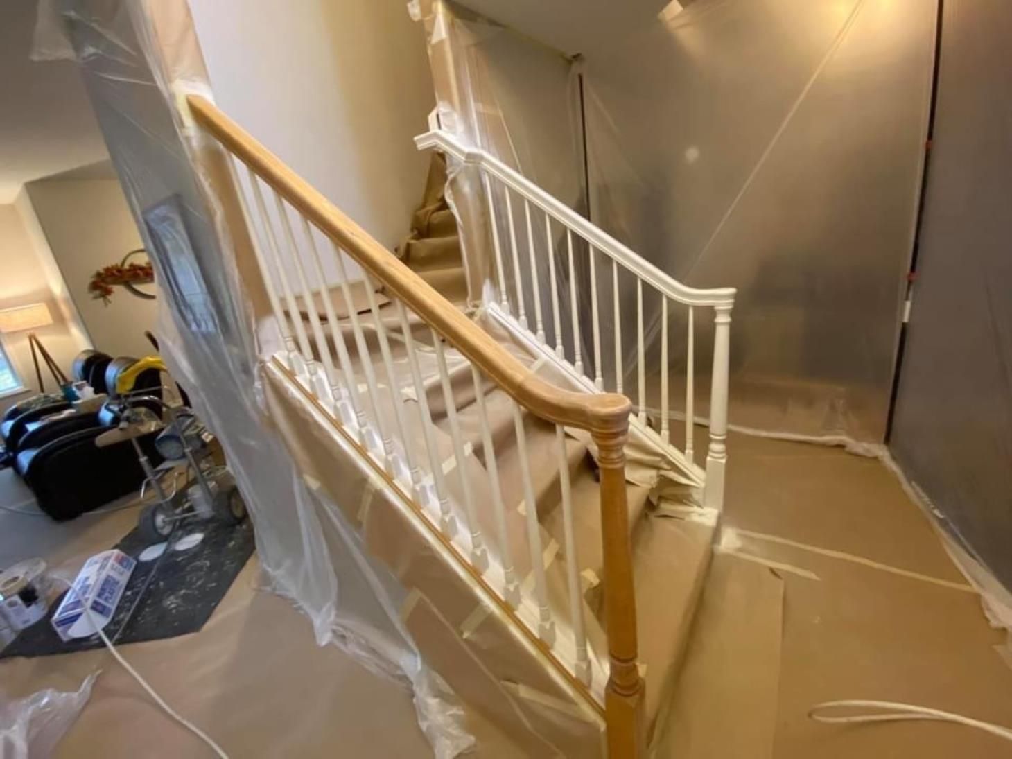 A staircase is being painted in a room with plastic covering it.
