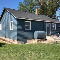 A blue house with a gas tank in the backyard.