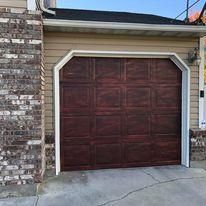 A brown garage door is sitting in front of a brick house.