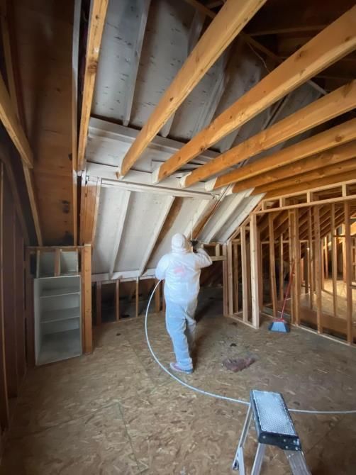 A man is spraying insulation on the ceiling of a house under construction