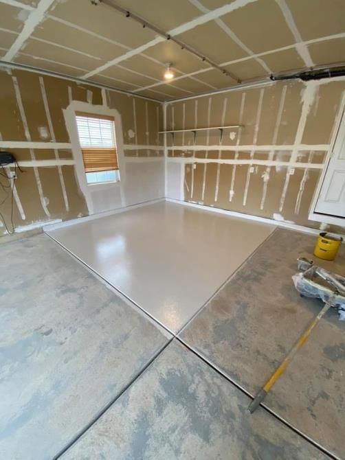 A garage that is being painted white with a broom on the floor