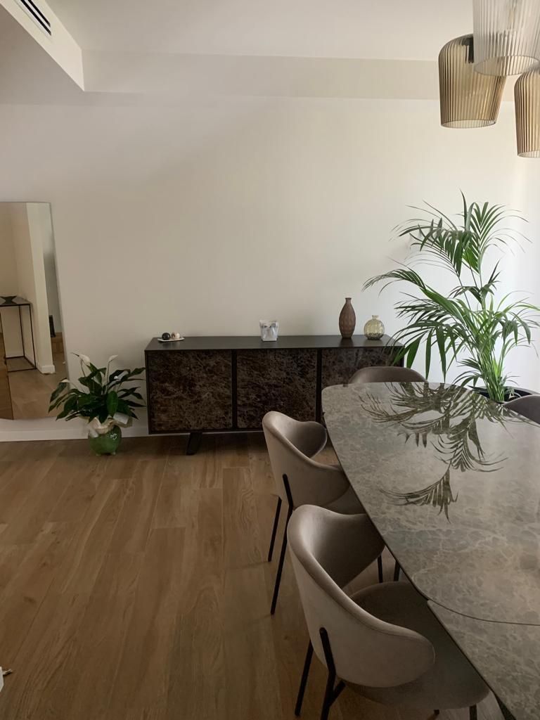 Sala da pranzo con pavimento in legno, tavolo ovale, sedie, buffet e una pianta in vaso.