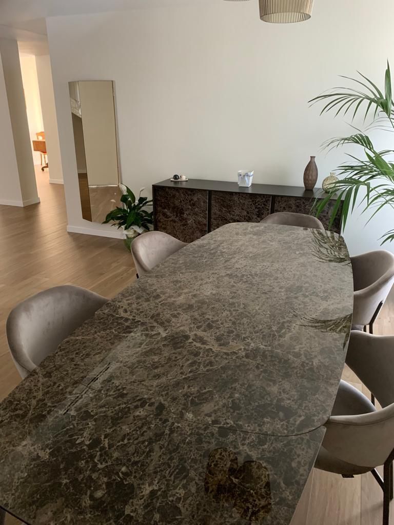 Sala da pranzo con grande tavolo in pietra, sedie e una credenza in legno scuro contro una parete bianca.