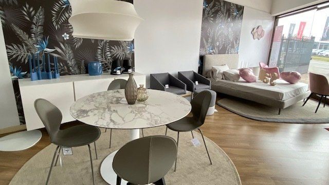 Zona pranzo in uno showroom di mobili con tavolo in marmo, sedie grigie e un'esposizione di oggetti d'arredo.