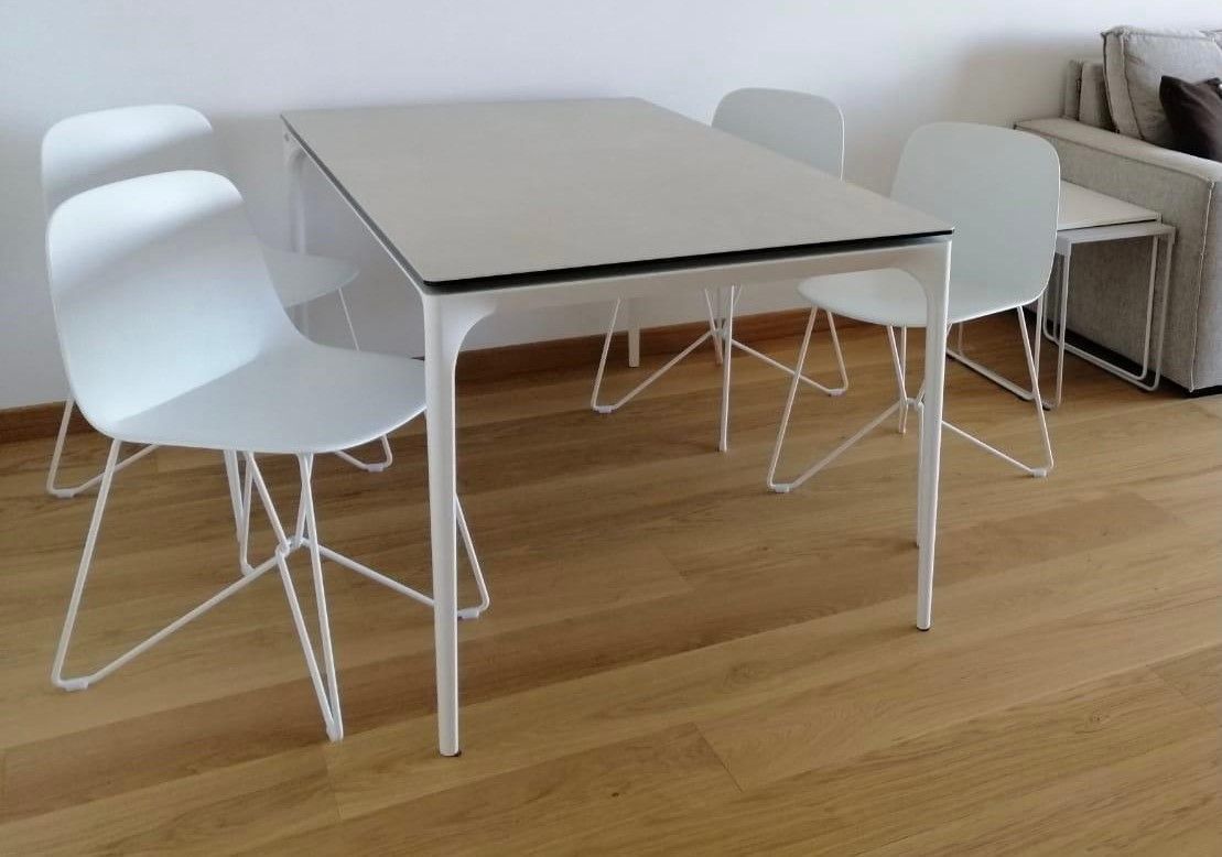 Tavolo e sedie bianchi su un pavimento in legno; sullo sfondo si intravede un divano.