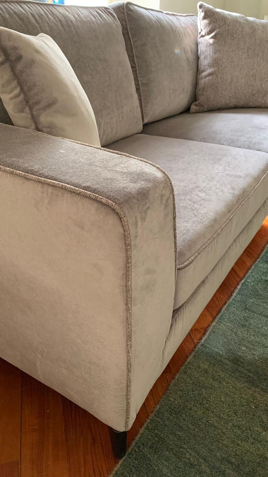 Divano grigio imbottito con tre cuscini e bracciolo.