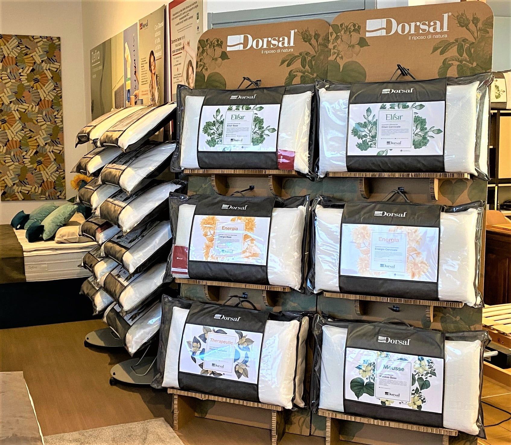 Cuscini esposti, impilati su scaffali di legno. Confezioni grigio scuro con etichette botaniche; marchio