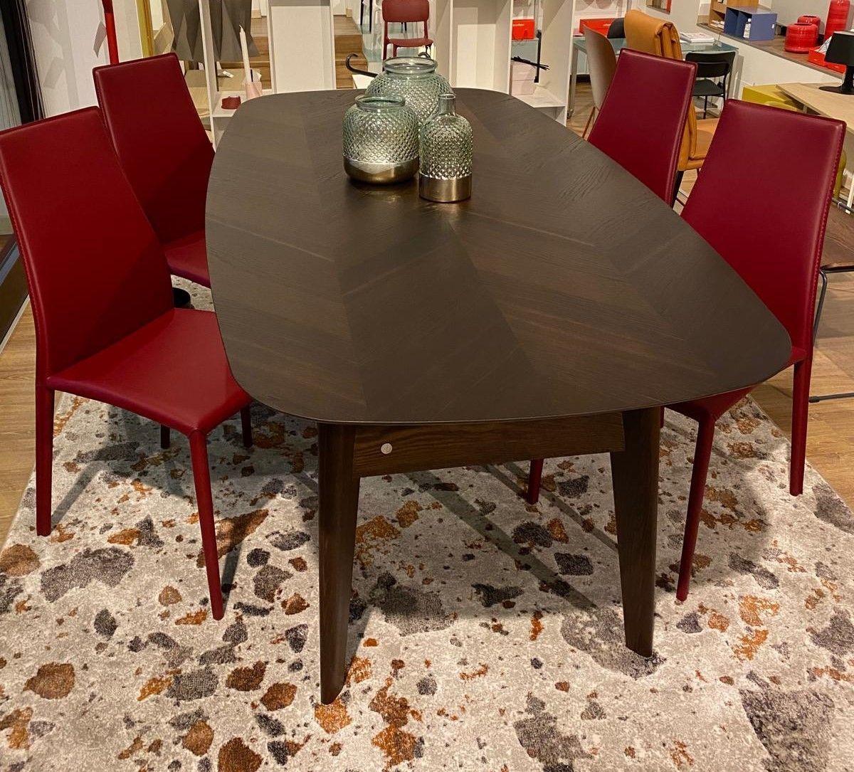 Tavolo da pranzo con quattro sedie rosse su un tappeto a fantasia. Tavolo in legno scuro, barattoli di vetro decorativi.