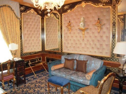 Lussuosa camera d'albergo con finiture dorate, divano blu e parete rivestita in velluto.