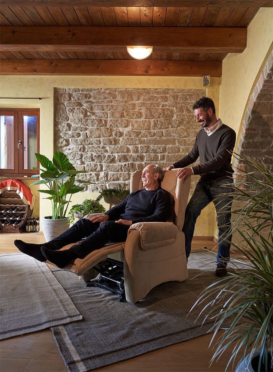 Un uomo è sdraiato su una poltrona beige, assistito da un altro uomo.