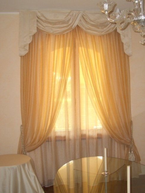 Tende trasparenti dorate incorniciano una finestra con una balza drappeggiata;