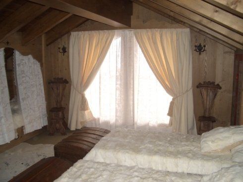 Accogliente camera da letto con soffitto in legno inclinato e finestra con tende color crema.