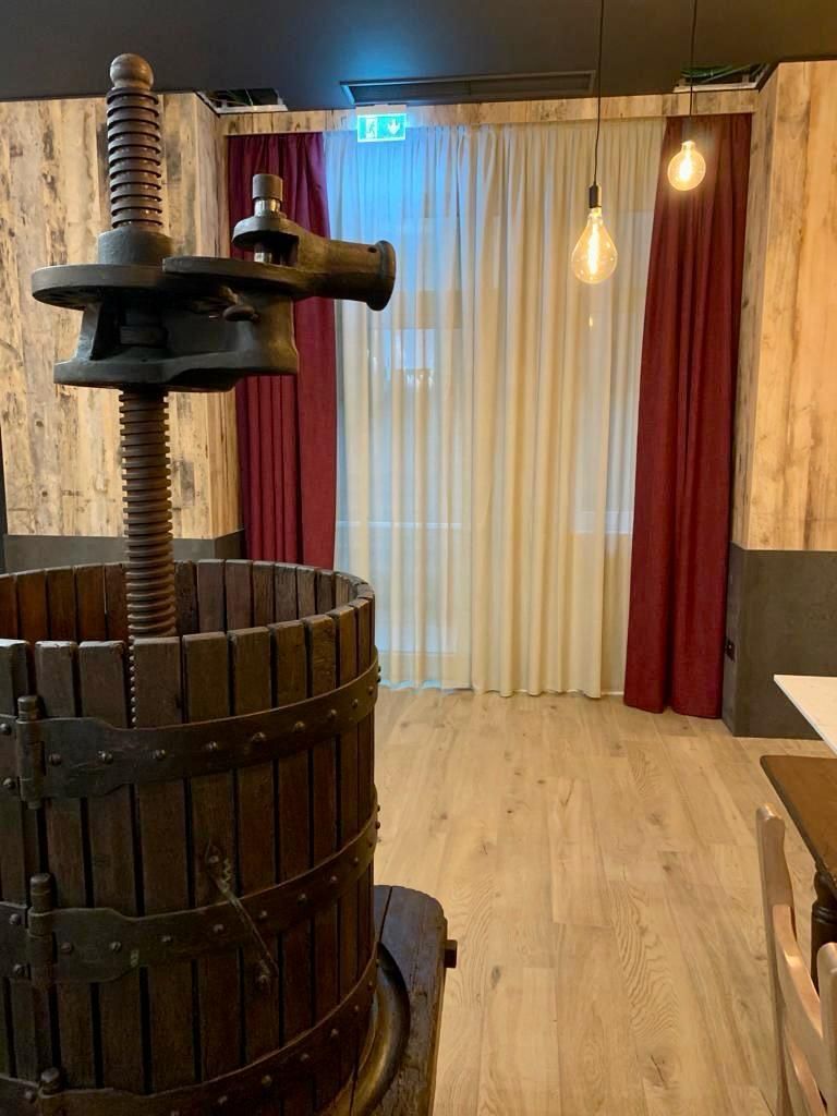 Torchio per il vino in legno all'interno di un ristorante con tende rosse e crema e luci sospese.