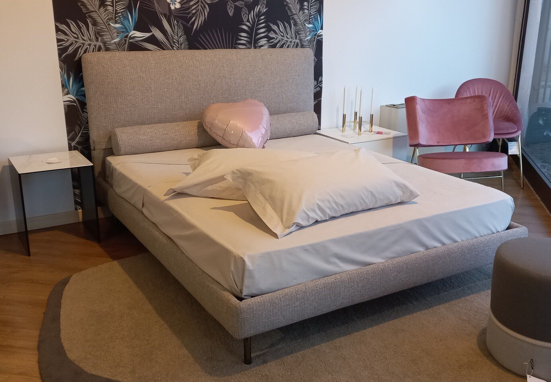 Un letto con una grande testiera, un tappeto rotondo e una sedia rosa.