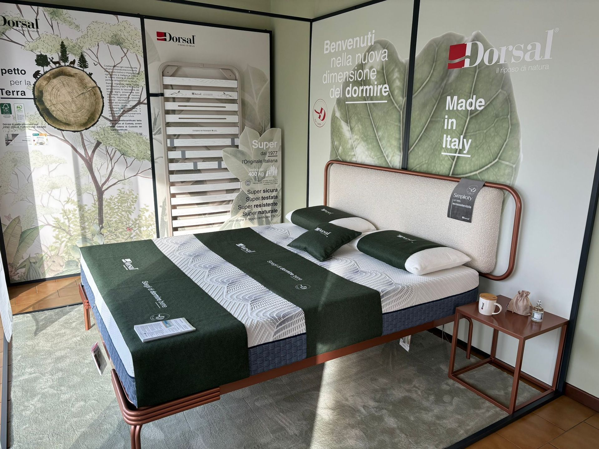 Espositore per camera da letto con materasso e struttura del letto Dorsal. Dettagli verdi e bianchi. Tavolino marrone.