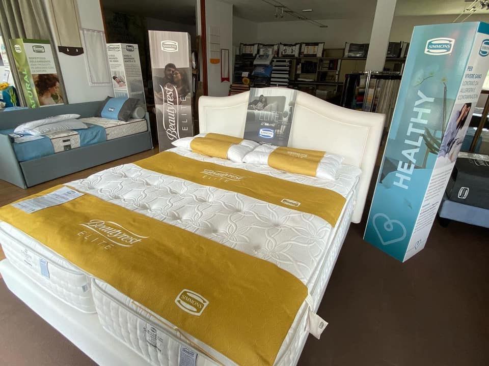 L'esposizione di materassi in un negozio presenta un grande letto bianco con dettagli dorati e la scritta 