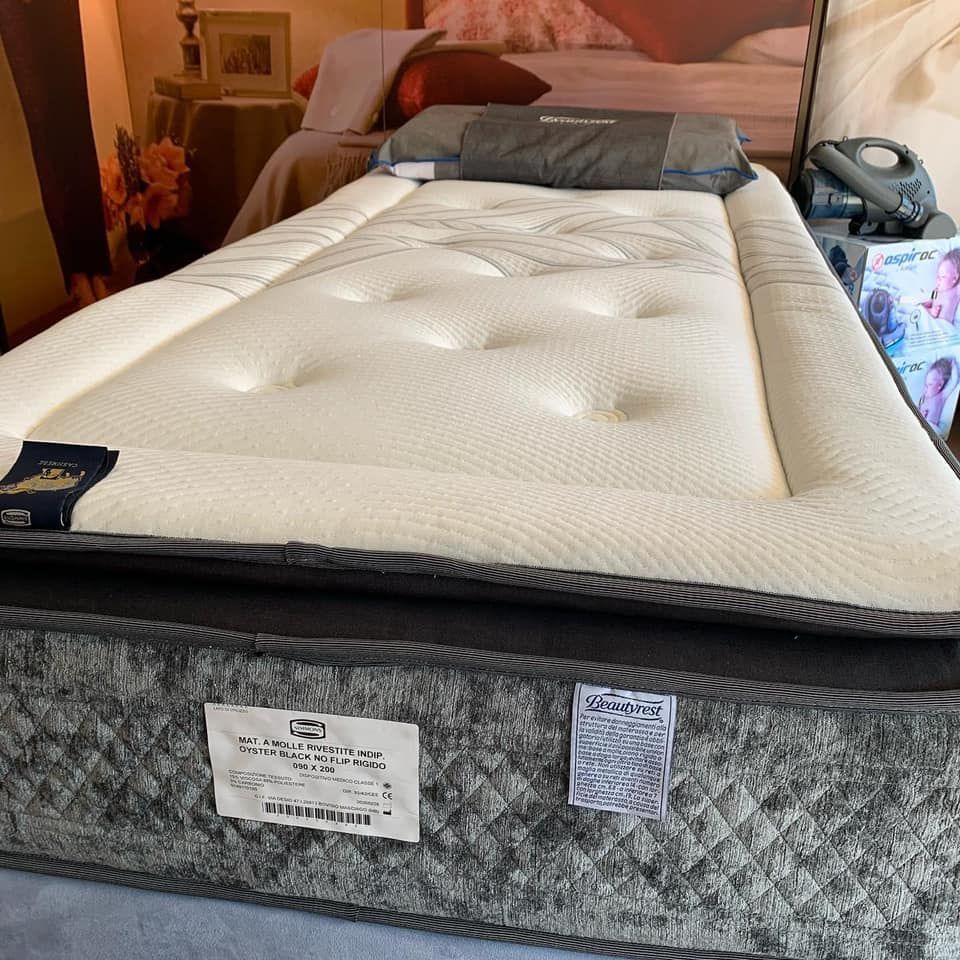 Un materasso per letto singolo con la parte superiore color crema e la base grigia, esposto in un negozio.