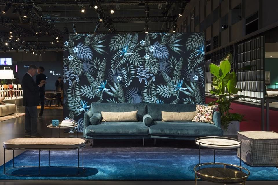 Esposizione del soggiorno con divano blu, carta da parati a fantasia e tavolini.