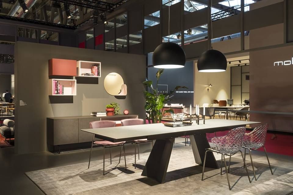 Sala da pranzo moderna con tavolo grigio, sedie trasparenti e lampade a sospensione nere.