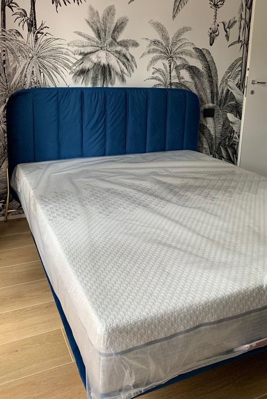 Letto imbottito blu con materasso bianco e carta da parati tropicale in bianco e nero.