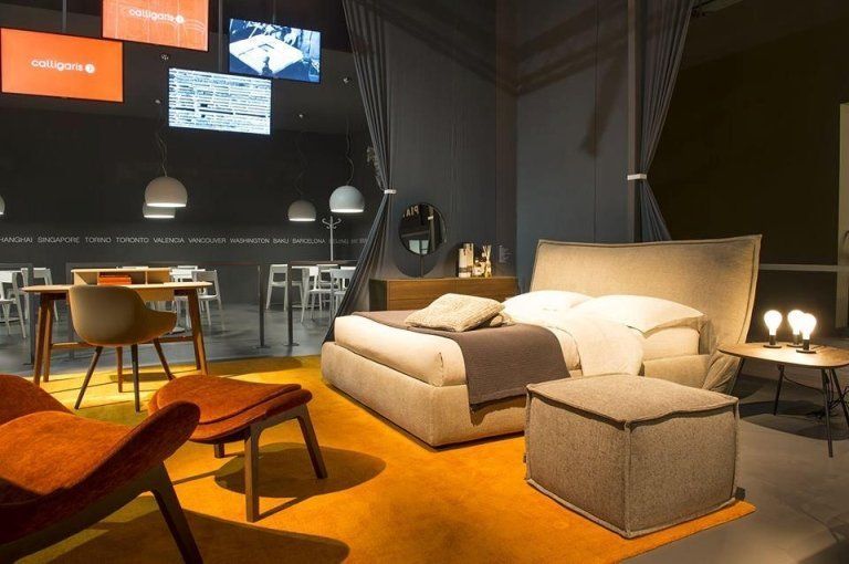 Una camera da letto moderna con letto, sedie e lampade. Tappeto arancione e mobili dai toni neutri.