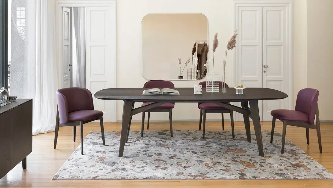 Sala da pranzo con tavolo in legno scuro, sedie viola e tappeto a fantasia.