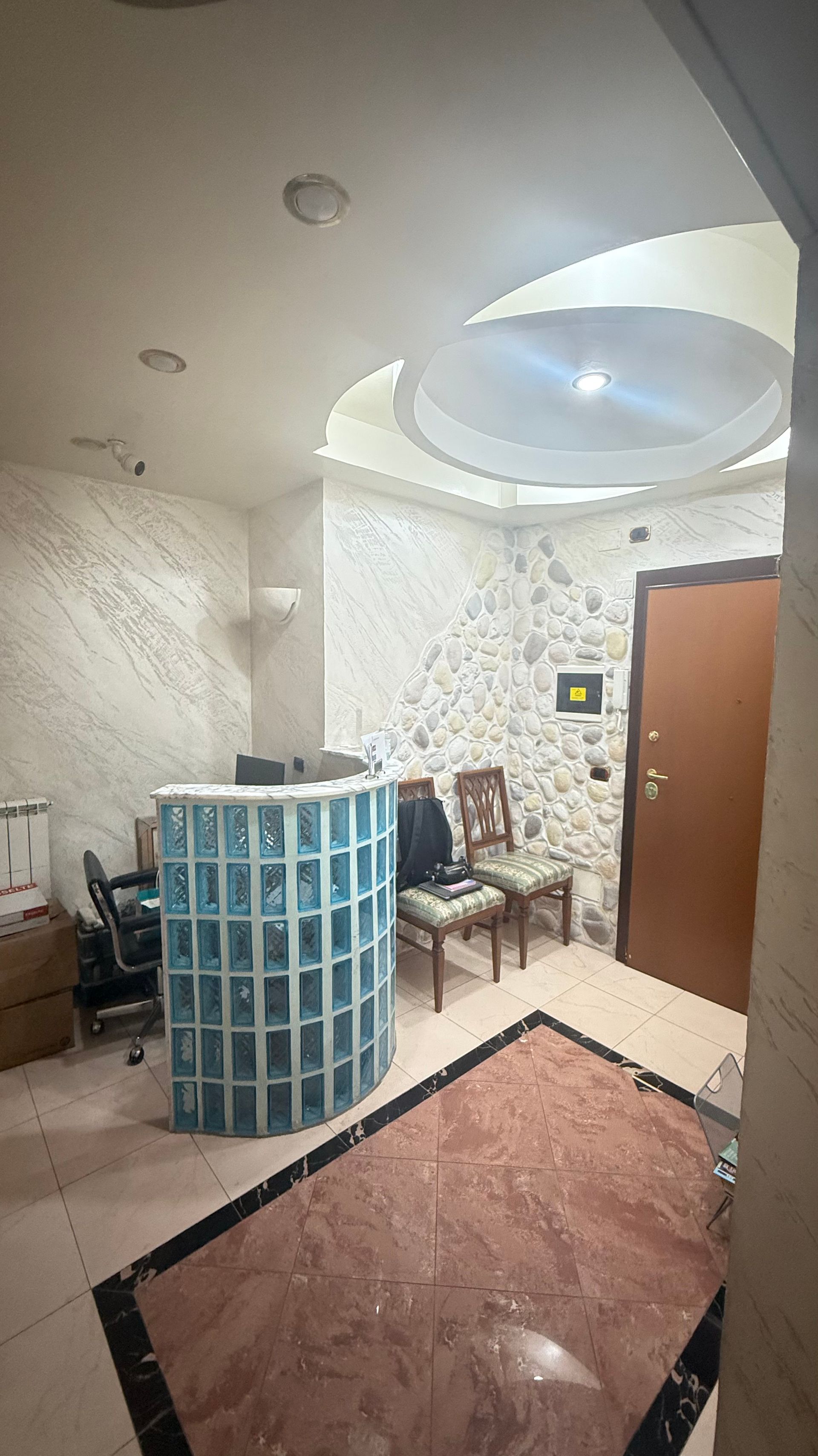 Area reception con scrivania in vetrocemento blu, porta marrone, parete in pietra e pavimento decorato.