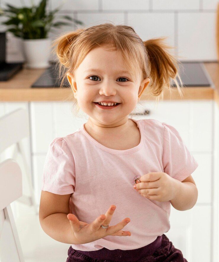 A little girl is sitting on a chair in a kitchen and smiling.