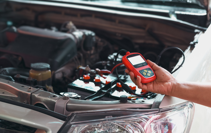 A person is holding a tool in front of a car with the hood open.
