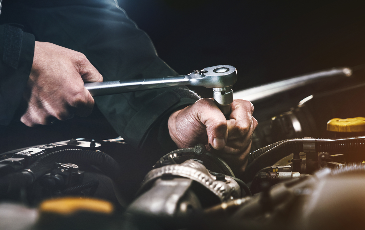 A man is working on a car engine with a wrench.