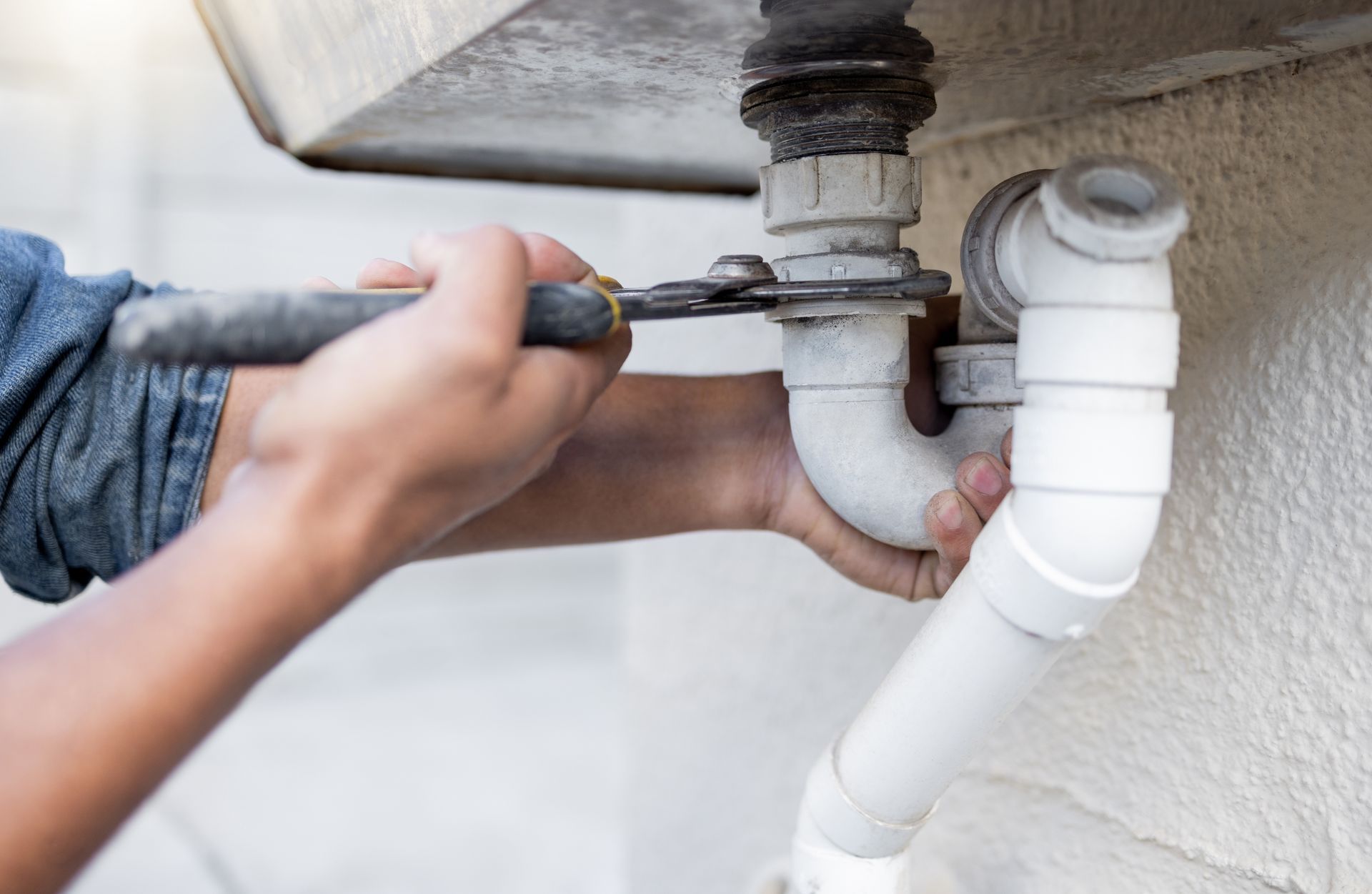 A plumber is fixing a pipe with a wrench.
