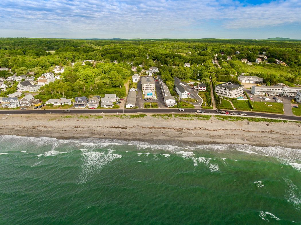 An aerial view of a beach with houses and trees in the background.