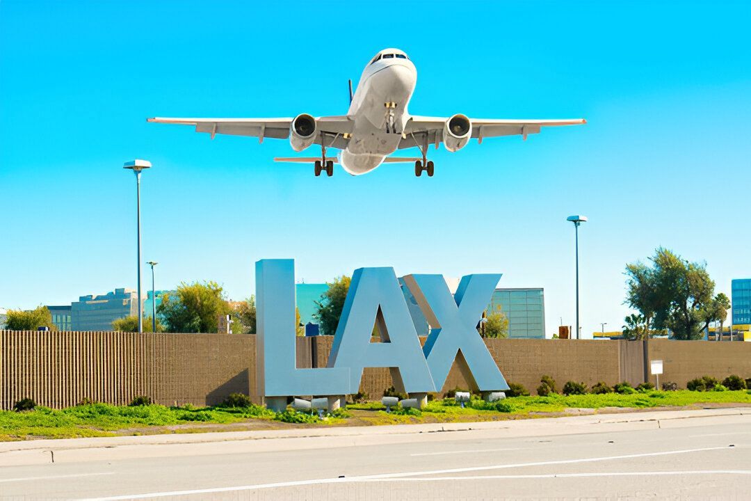 Airplane taking off over the LAX airport sign on a sunny day.