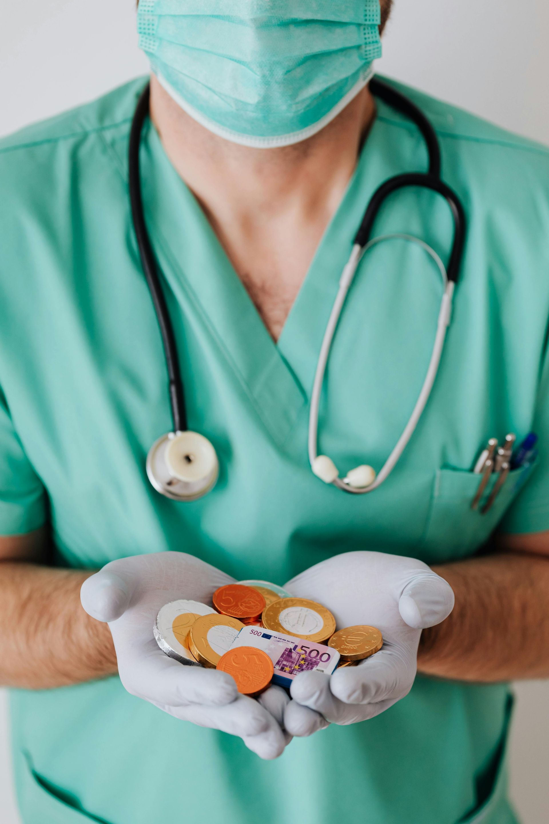 A doctor wearing a mask and stethoscope is holding coins in his hands.