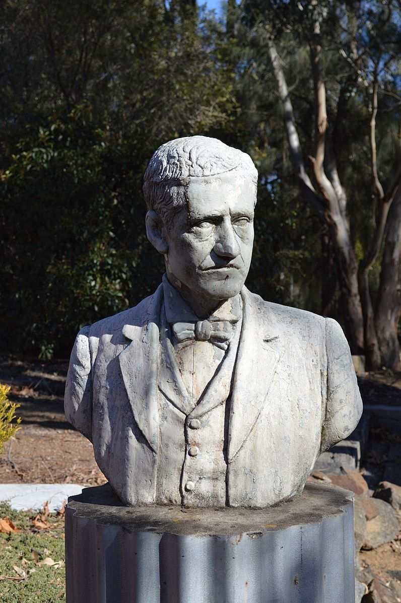A statue of a Banjo Paterson in a suit and bow tie is sitting on top of a metal pillar.