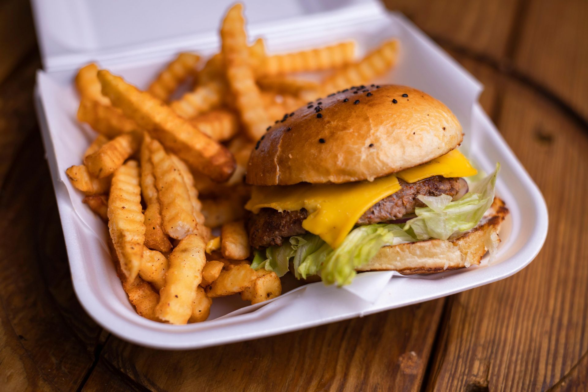 A hamburger and french fries in a styrofoam container on a wooden table.