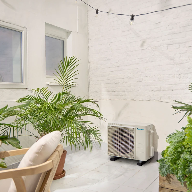 Unità di aria condizionata esterna sul patio con piante e luci a stringa.