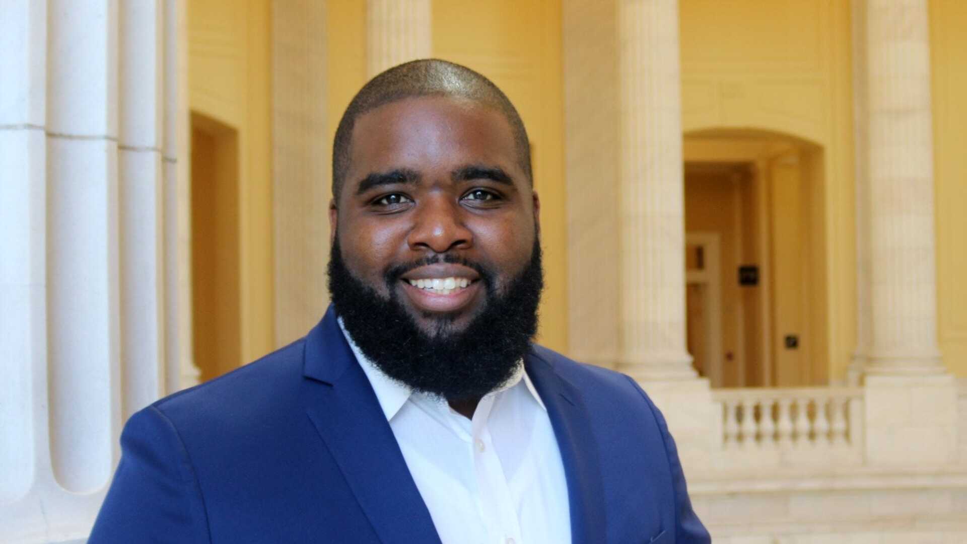 A man with a beard is wearing a blue suit and white shirt.