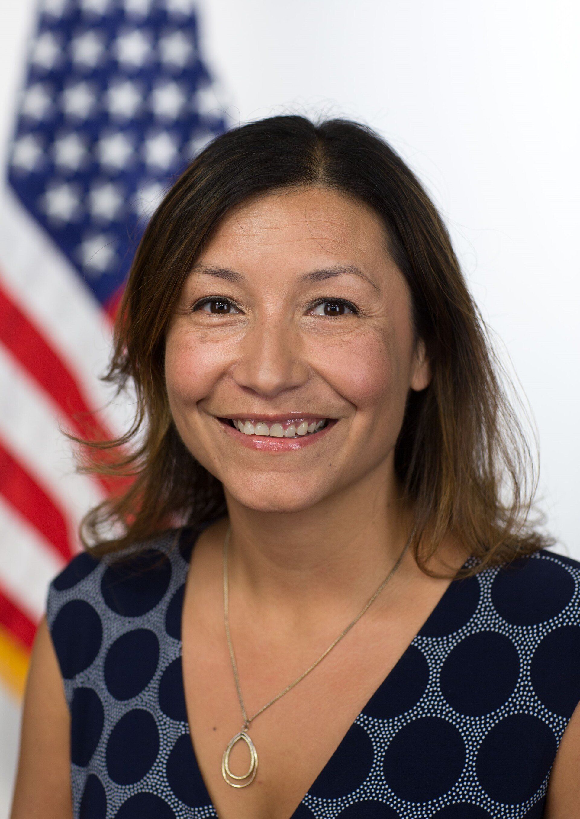 A woman is smiling in front of an american flag.