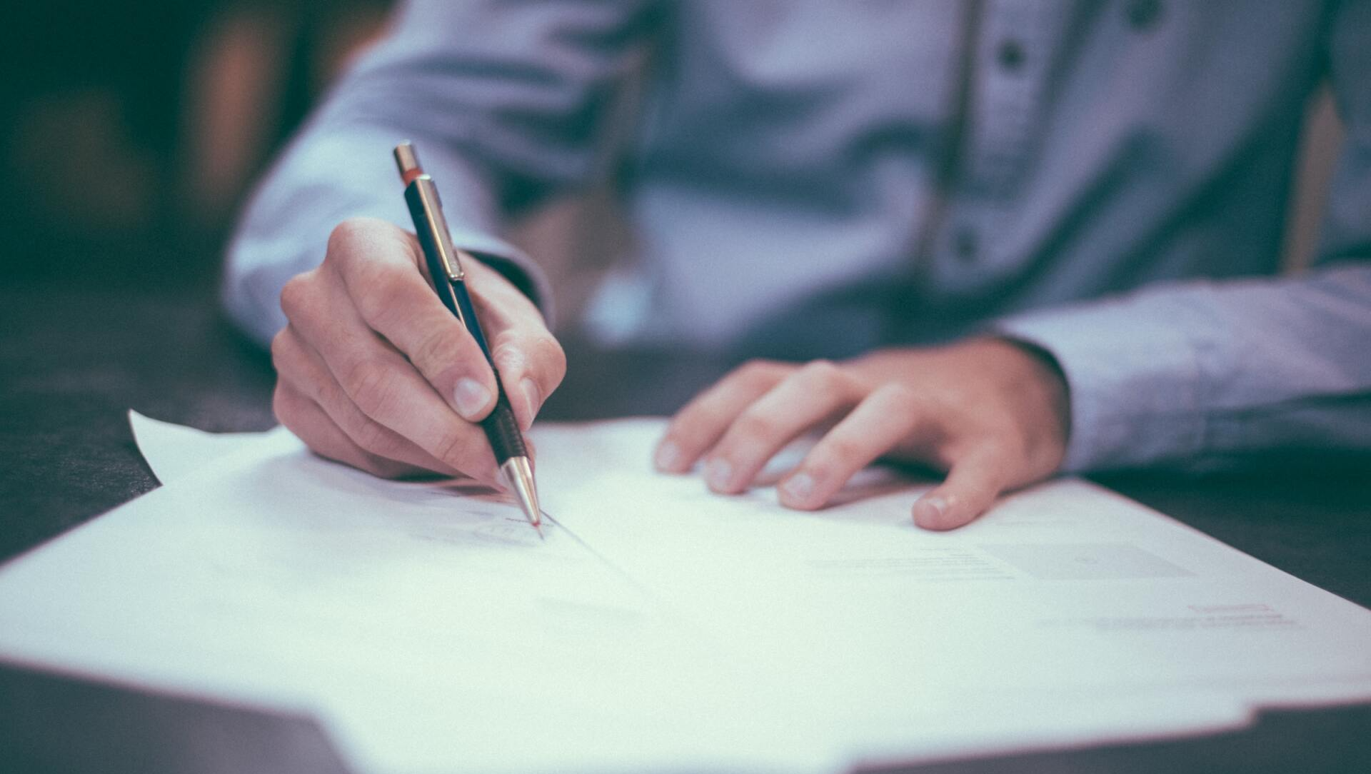 A man is writing on a piece of paper with a pen.