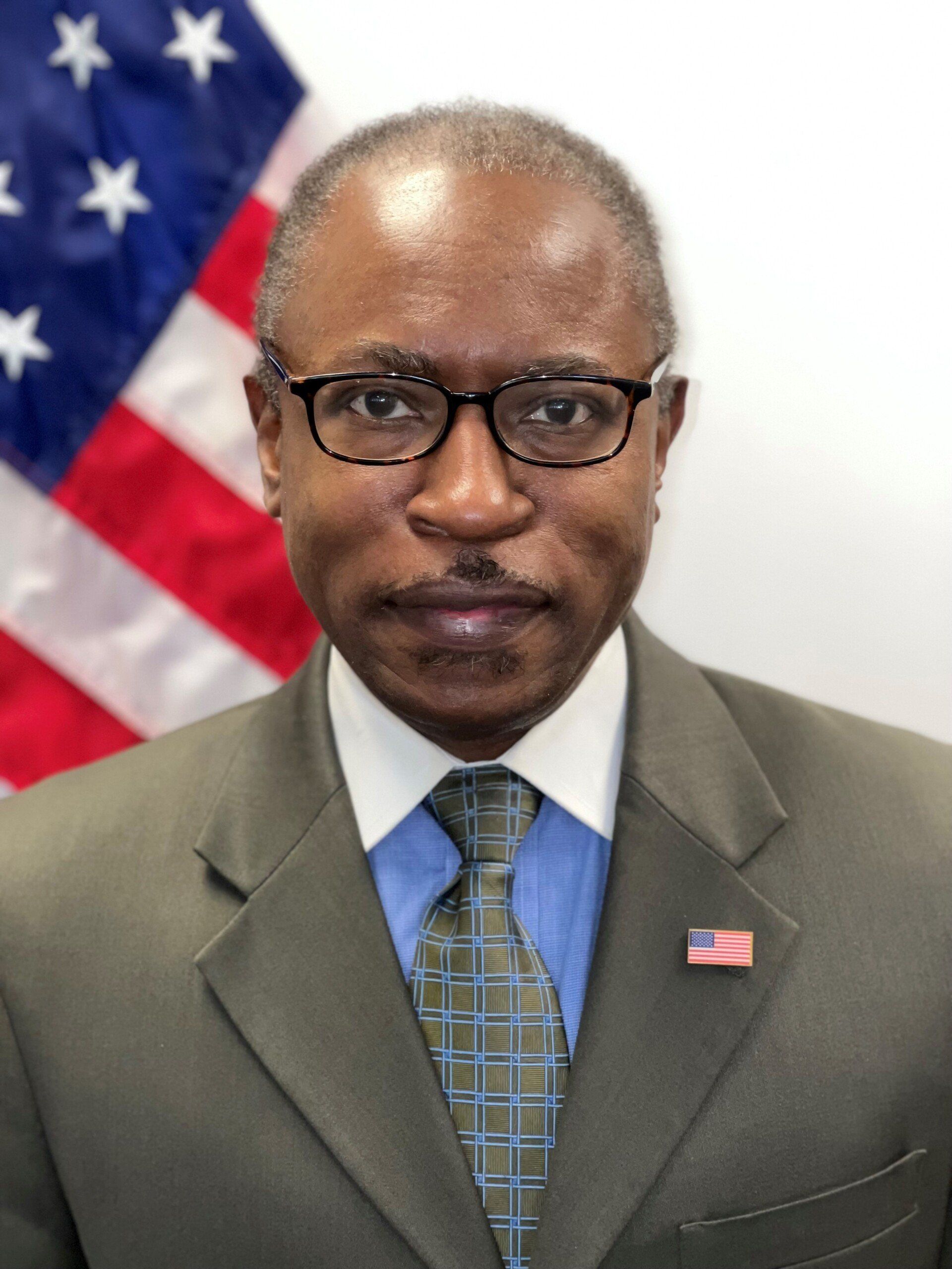 A man in a suit and tie is standing in front of an american flag.