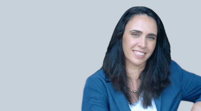 A woman with long dark hair is wearing a blue jacket and smiling.