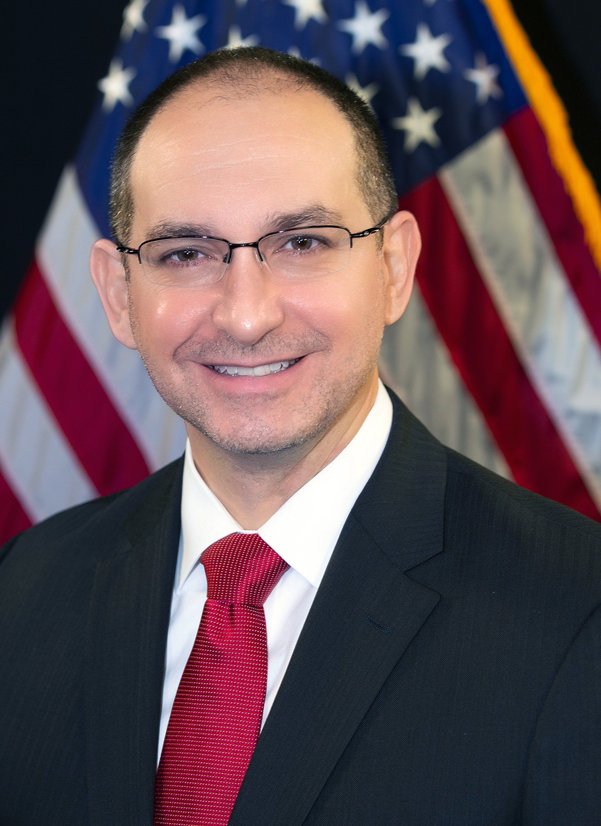 A man in a suit and tie is smiling in front of an american flag