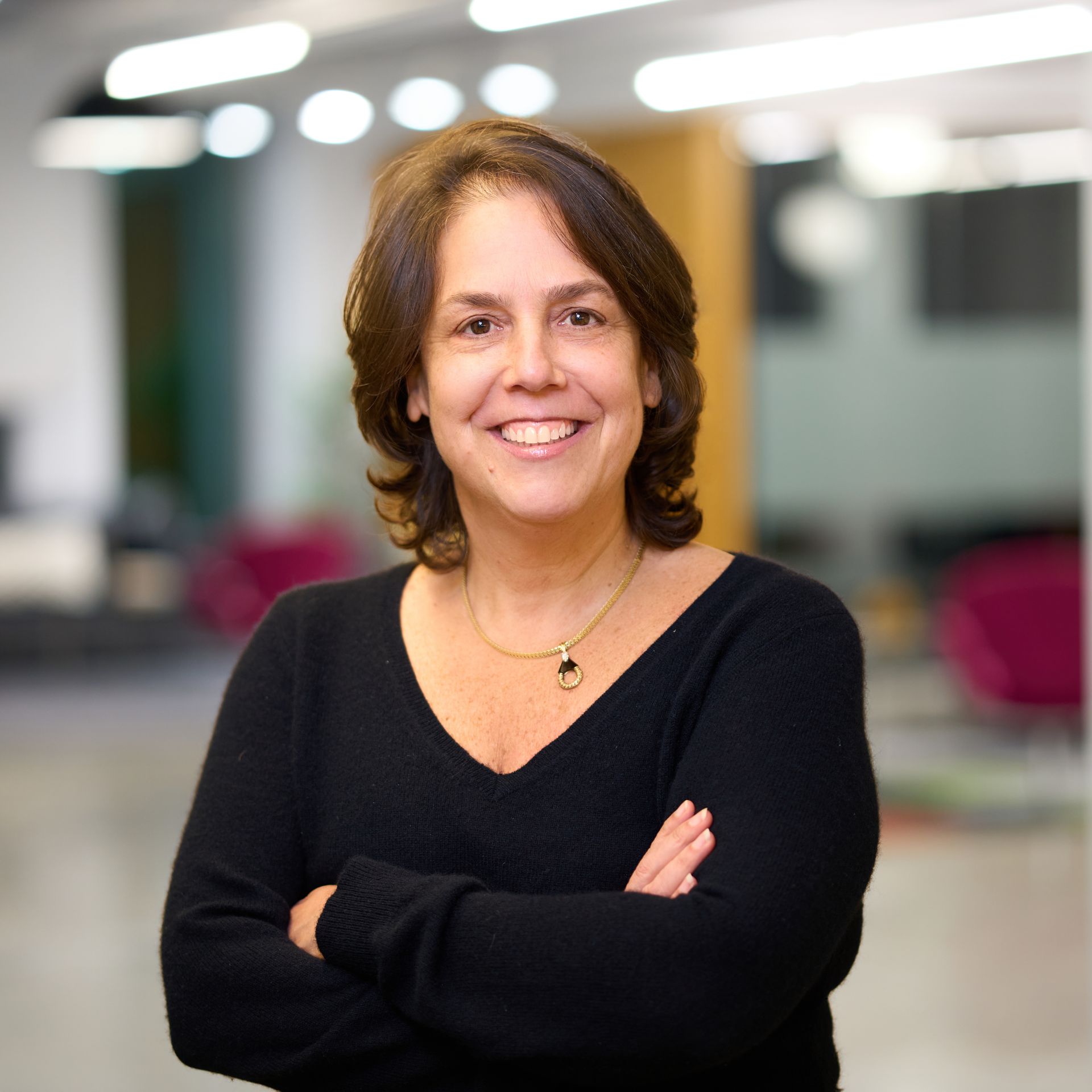 A woman in a black shirt with folded arms smiles in front of a blurred office background.