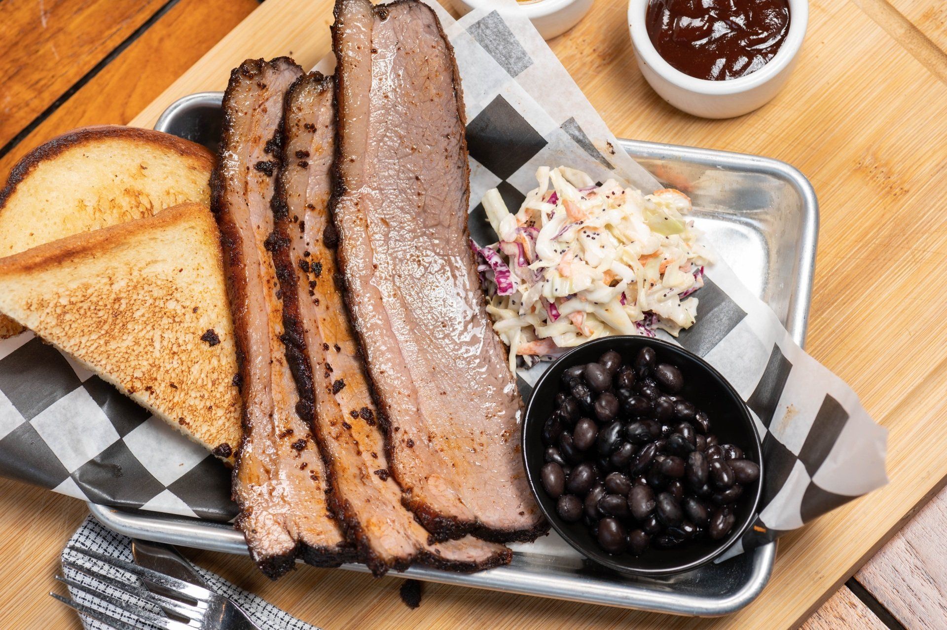 A plate of meat , beans , coleslaw and toast on a wooden table.